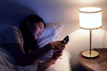 Blaues Licht, Wirkung und Schutz. Zu sehen ist eine junge Frau, die im Bett liegt und auf ihrem Handy liest.