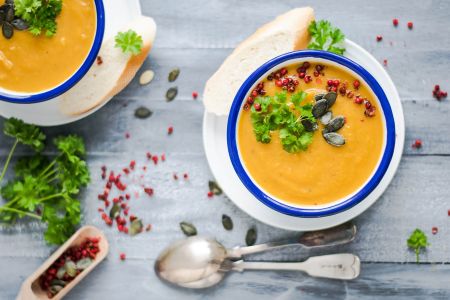 Wärmende Lebensmittel nach TCM und Ayurveda: zu sehen sind zwei Schalen mit Suppe, dekoriert mit Petersilie, Granatapfelkernen und Kürbiskernen
