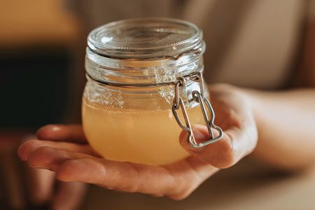 Selbst gemachter Sauerhonig in einem Einmachglas, gehalten auf einer ausgestreckten Hand