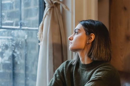 Junge, nachdenkliche Frau am Fenster: Burnout oder Erschöpfung?