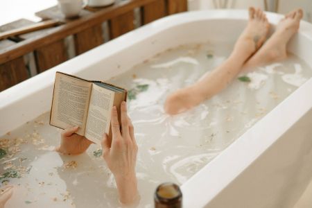Mehr Ruhe im Alltag: baden gehen. Zu sehen ist eine Badewanne, eine Person liegt im Wasser und liest ein Buch.