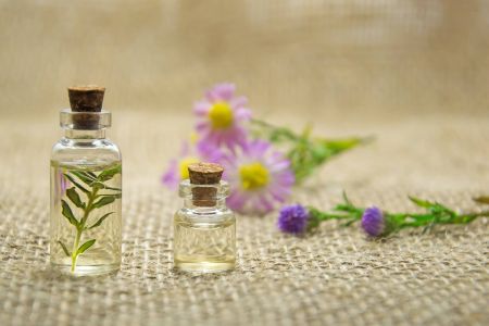 Aromapflege zuhause: Wickel, Auflagen und Aromabäder. Zu sehen sind zwei kleine Gasflaschen mit Öl. Zu r Deko liegen Blumen im Hintergrund.
