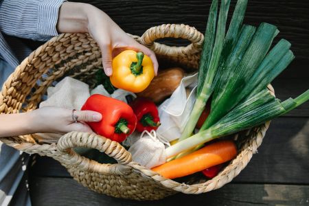 Vitalstoffe für das Immunsystem: eine Frau hält 2 Paprika über einem geflochtenen Einkaufskorb. Im Korb sind noch Möhren, Lauch und ein Kürbis